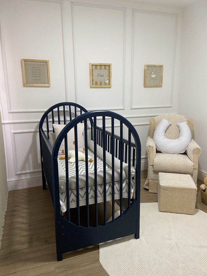 Quarto com berço azul e três quadros bordados na parede