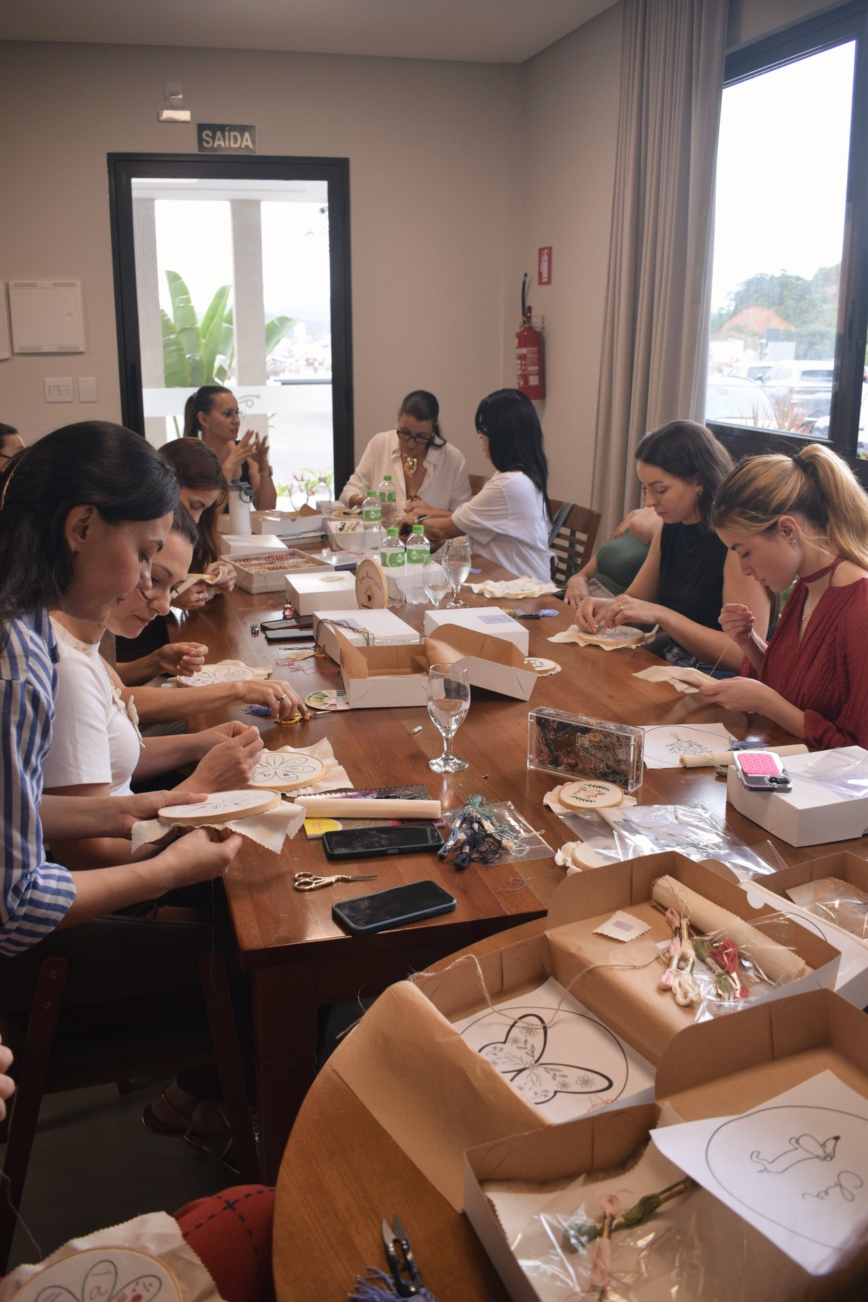 Turma bordando ao redor da mesa, cada pessoa com seu bastidor